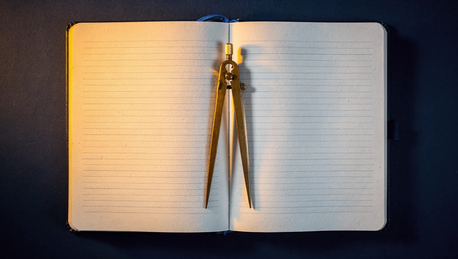 An open blank logbook with a brass dividers instrument, lit in amber on deep navy